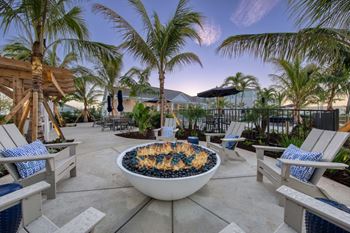 a patio with palm trees and chairs and a fire pit